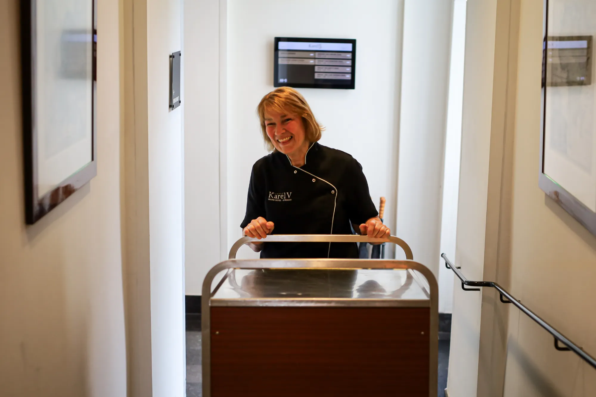 Medewerkster lacht terwijl ze een serveerwagen duwt

